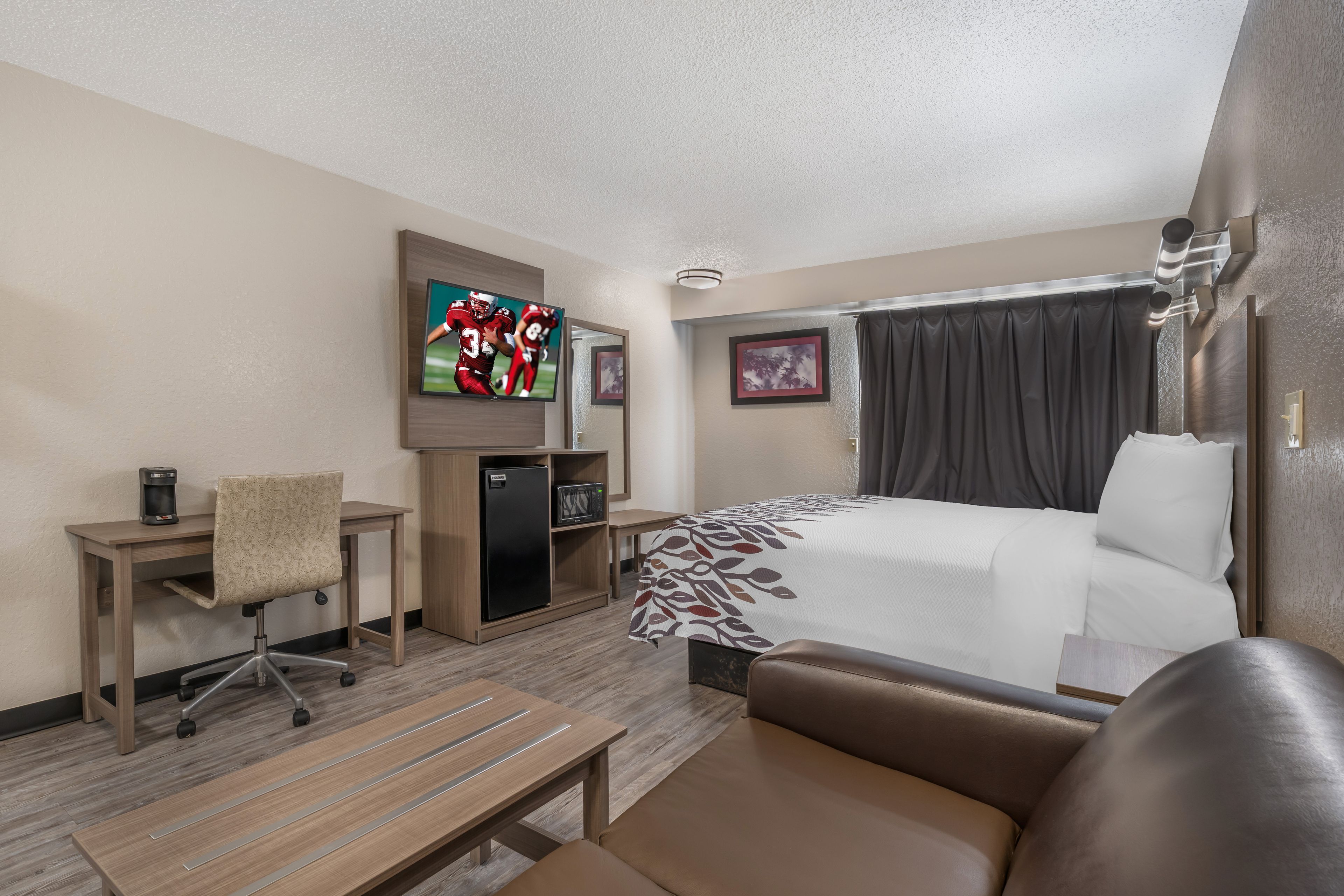 A hotel room with a bed, a desk, a chair, a television, and a refrigerator.