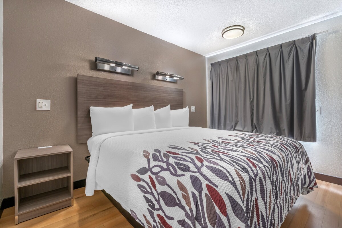 A modern hotel room with a large bed, a bedside table, and a headboard with integrated lighting.