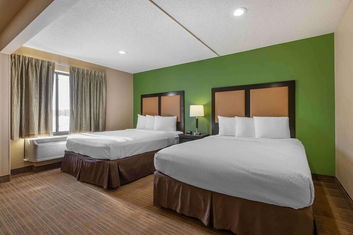 Ein Hotelzimmer mit zwei Betten, einem Fenster mit Vorhängen, einer Lampe und einem Thermostat.