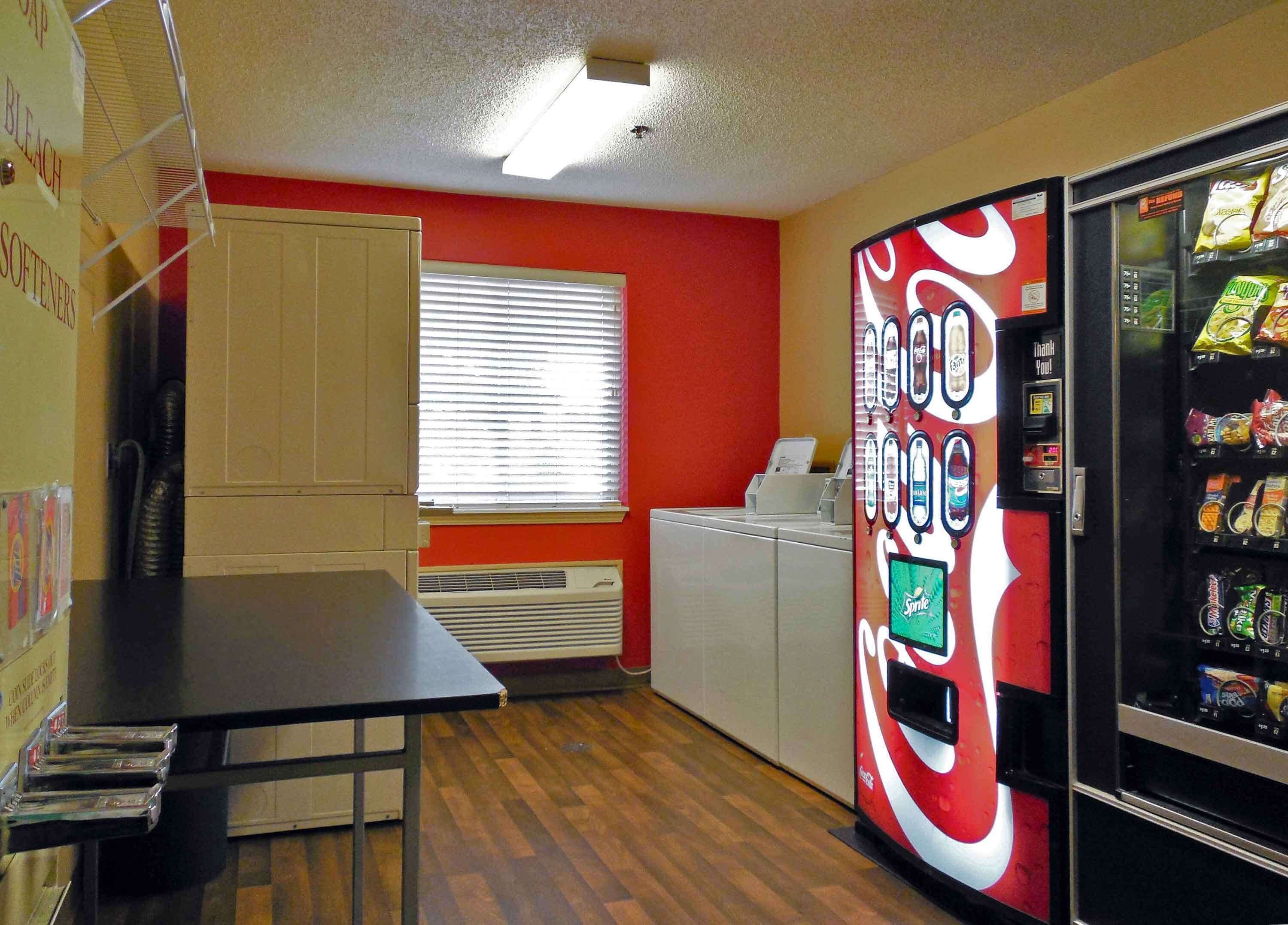 Una cocina pequeña con un refrigerador, una máquina expendedora y una ventana con persianas.