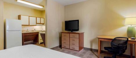 A hotel room with a bed, a desk with a chair, a television, a dresser, and a kitchenette.