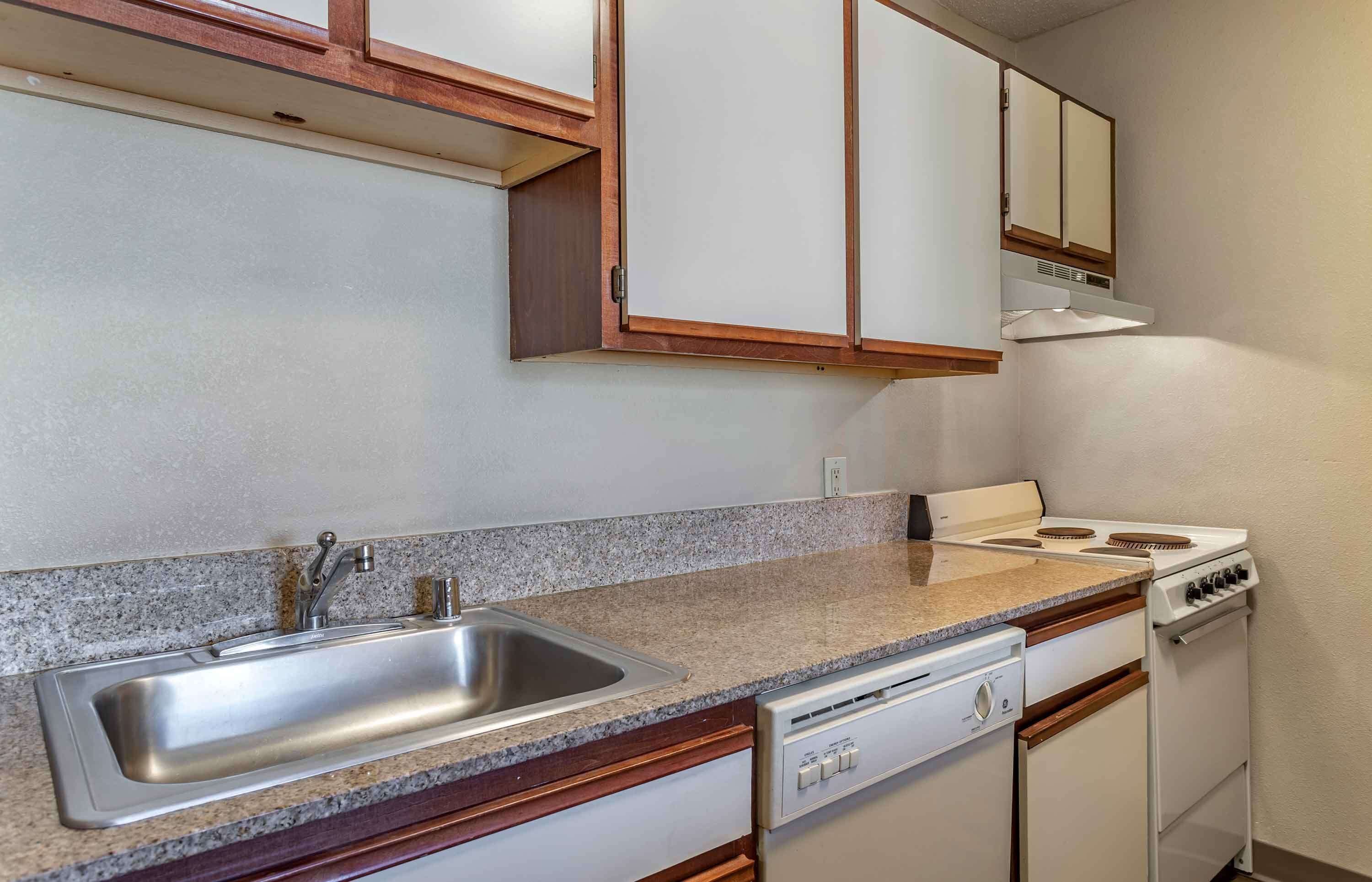 Una cocina con encimera de granito, pileta de acero inoxidable, muebles blancos y estufa blanca.
