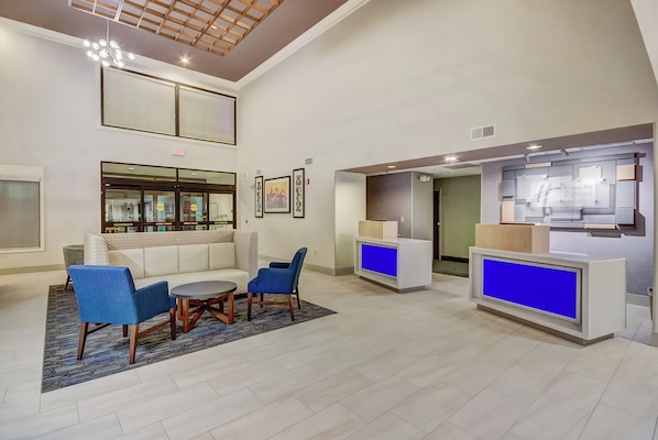 Un vestíbulo de hotel con mostrador de recepción, zona de estar y un techo alto con diseño de madera.