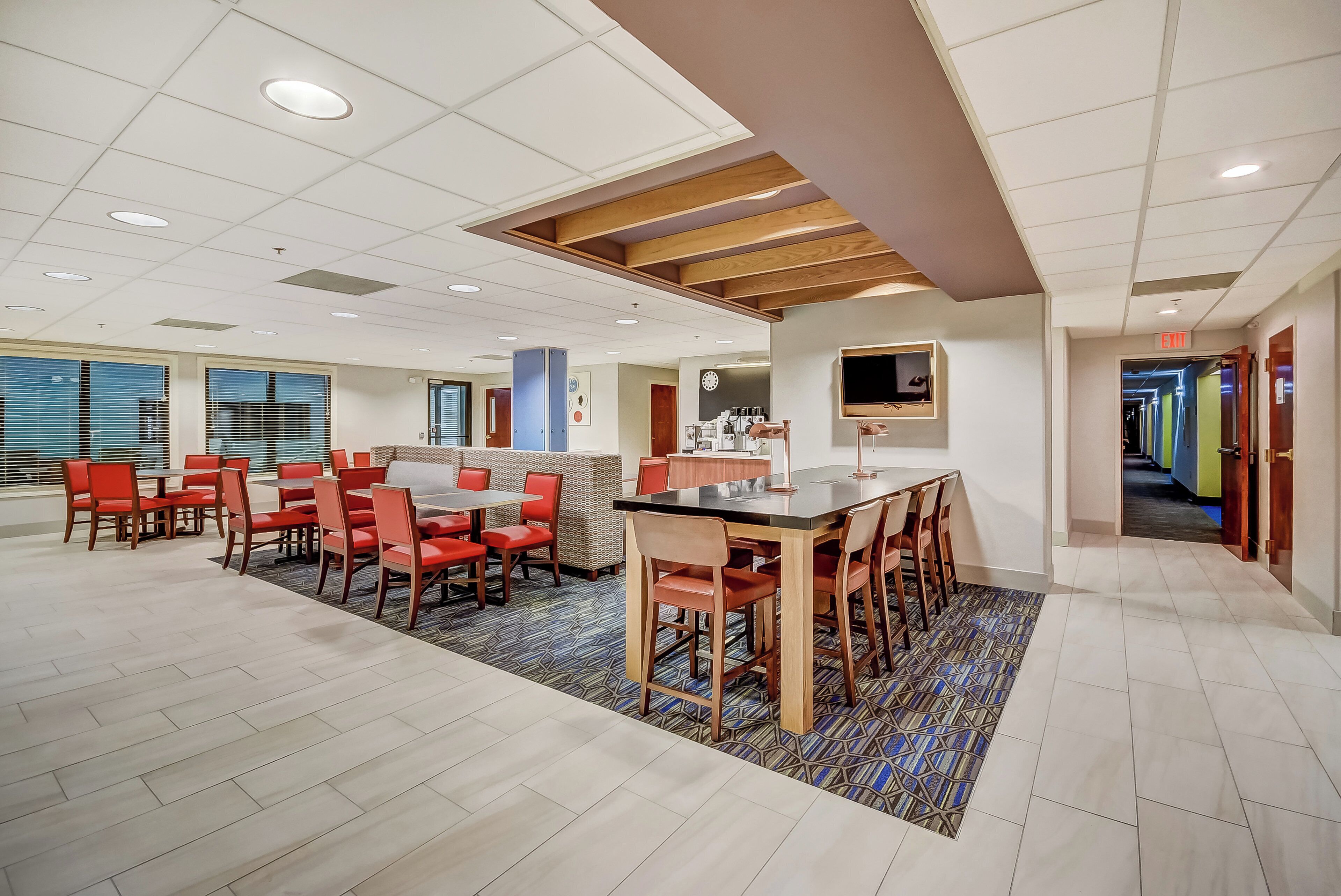 Une salle de conférence moderne dans un hôtel, avec une grande table, des chaises rouges et un tapis à motifs.