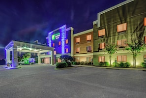 Edificio de Holiday Inn Express & Suites con una entrada bien iluminada y un estacionamiento.