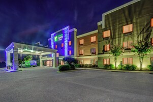 Edificio de Holiday Inn Express & Suites con una entrada bien iluminada y un estacionamiento.