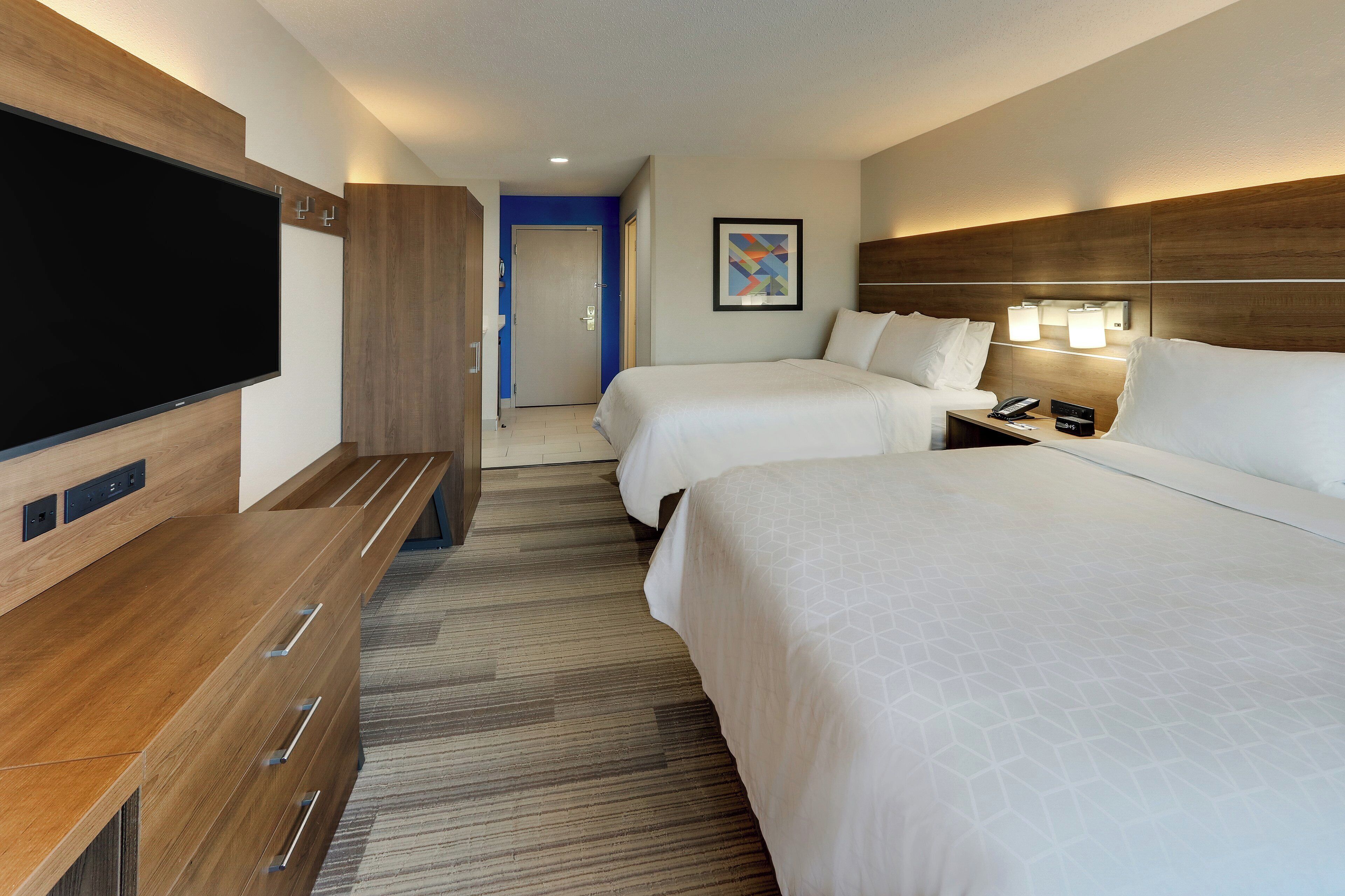 A hotel room with a TV, a desk, two beds, a nightstand, and a bathroom.