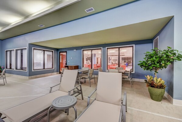 A spacious indoor seating area with tables and chairs, large windows with blinds, and a potted plant. - Holiday Inn Express & Suites Greenville Airport by IHG (Greer)