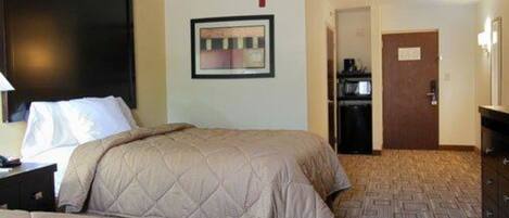 A hotel room with a bed, a desk with a lamp, a microwave, and a door.