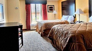 A hotel room with two beds, a desk, and a window with red curtains. - Quality Inn & Suites Greenville near downtown (Greenville)