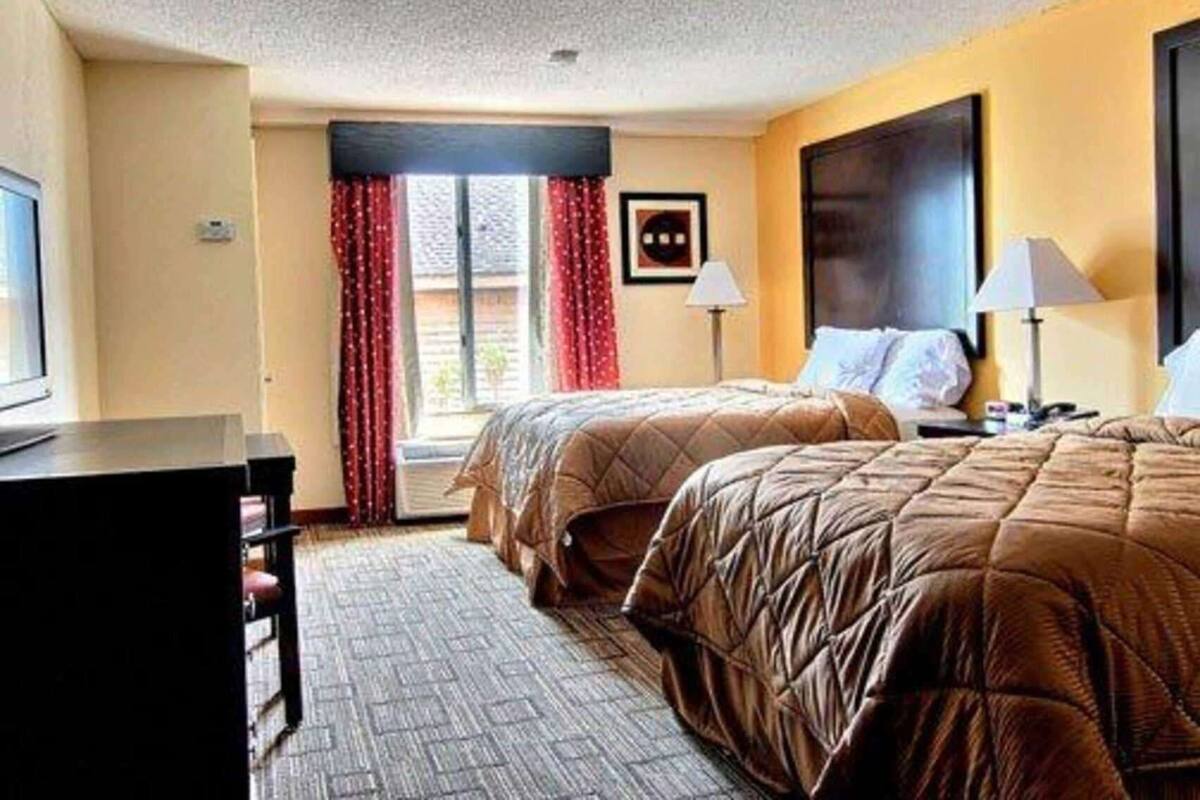 A hotel room with two beds, a desk, and a window with red curtains.