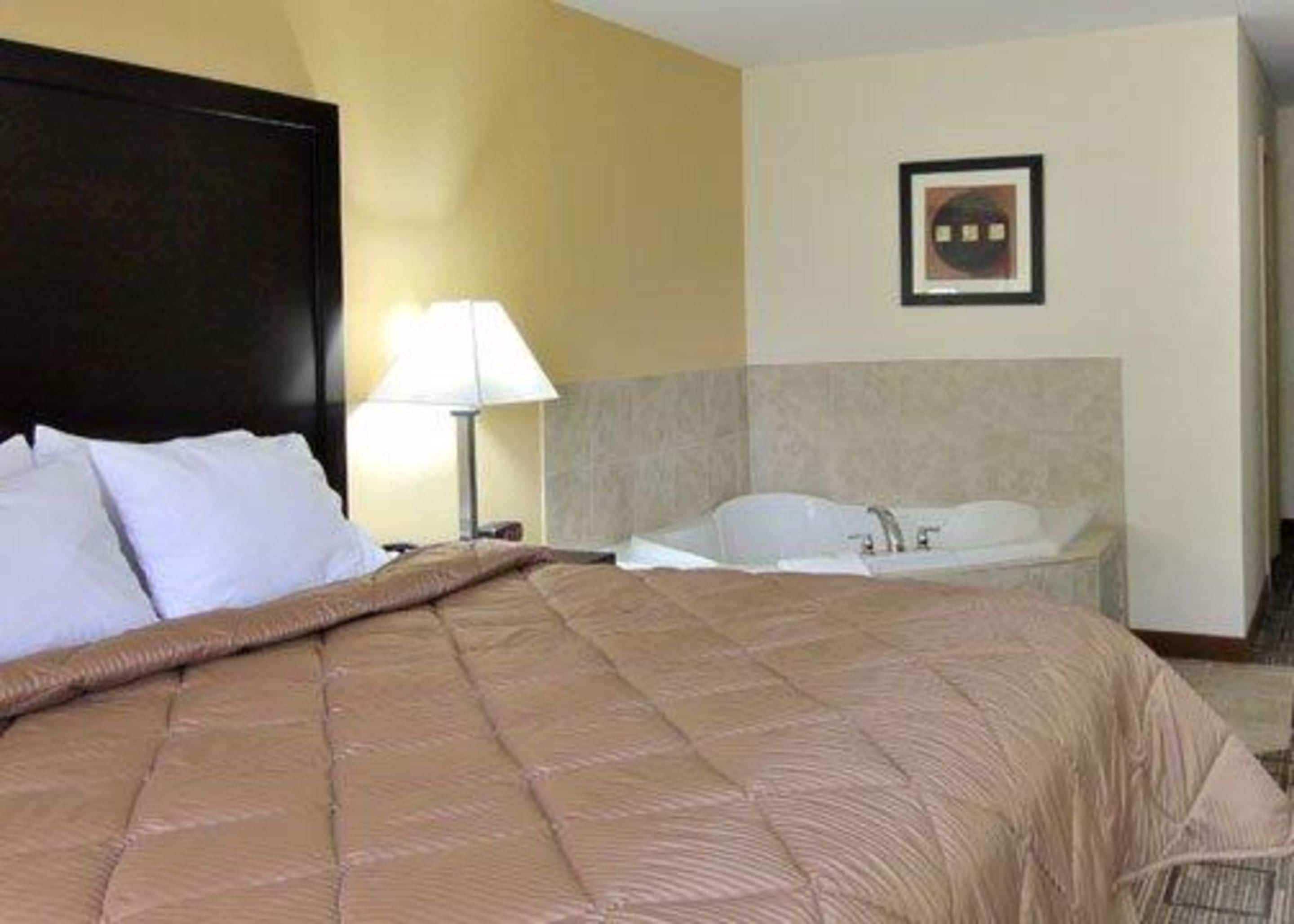 A hotel room with a large bed, a nightstand, a lamp, and a bathtub.