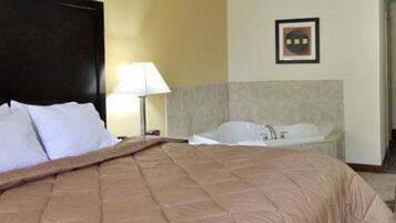 A hotel room with a large bed, a nightstand, a lamp, and a bathtub.