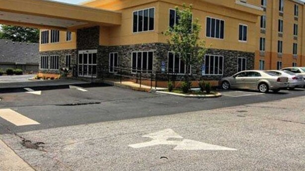 A multi-story hotel with a yellow facade, a covered parking area, and a visible parking sign. - Quality Inn & Suites Greenville near downtown (Greenville)