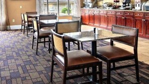 A hotel room with a dining area, a kitchen with wooden cabinets, and a large window providing a view of the outdoors. - Quality Inn & Suites Greenville near downtown (Greenville)