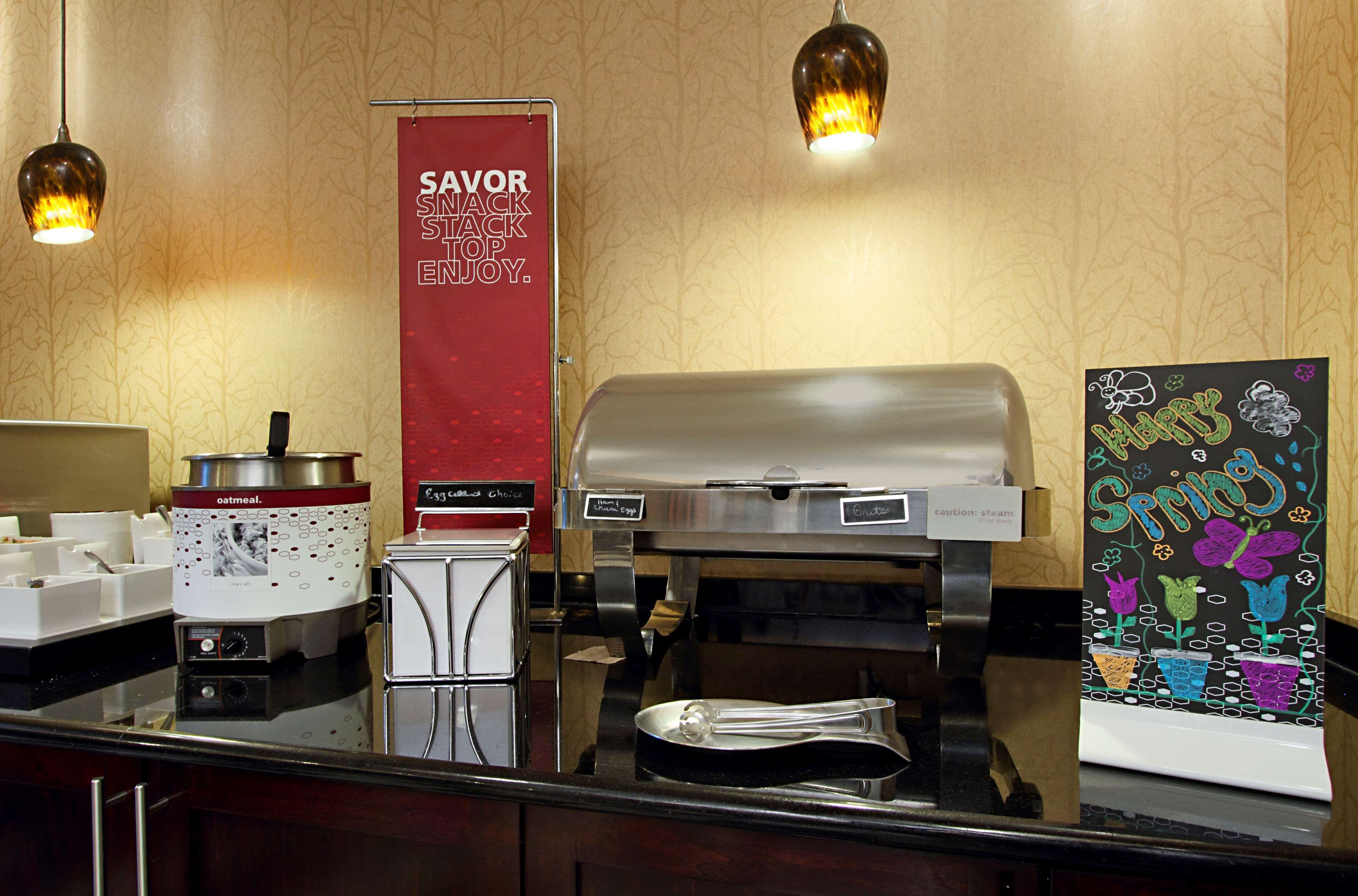 A breakfast station with a coffee maker, an oatmeal dispenser, and a sign that reads "SAVOR SMACK STACK ENJOY."
