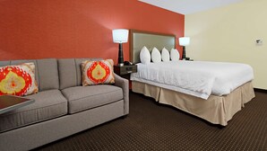 A hotel room with a bed, a sofa, two lamps, and a nightstand.