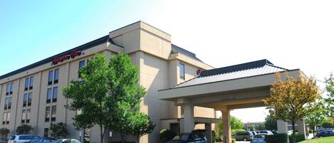 A hotel with a covered entrance, multiple parking spaces, and a clear sky.