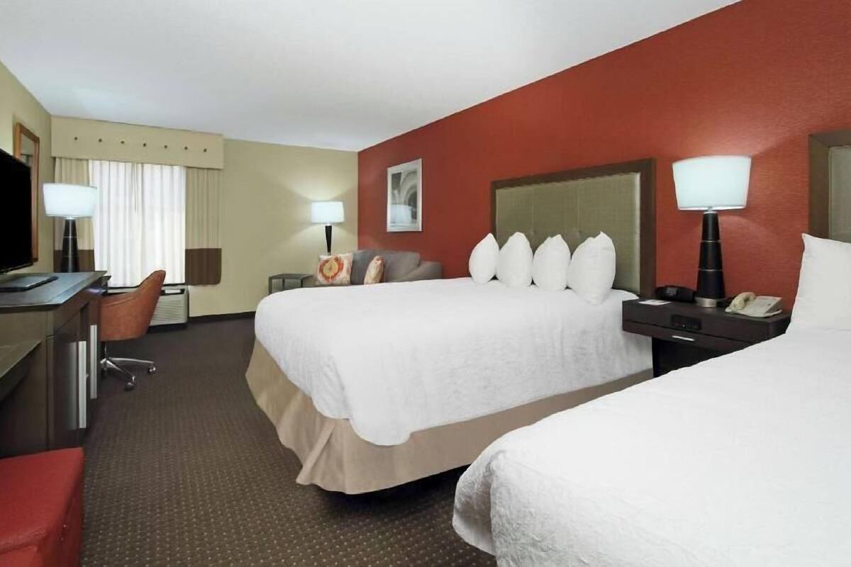 A hotel room with two beds, a desk, a chair, a television, and a lamp.