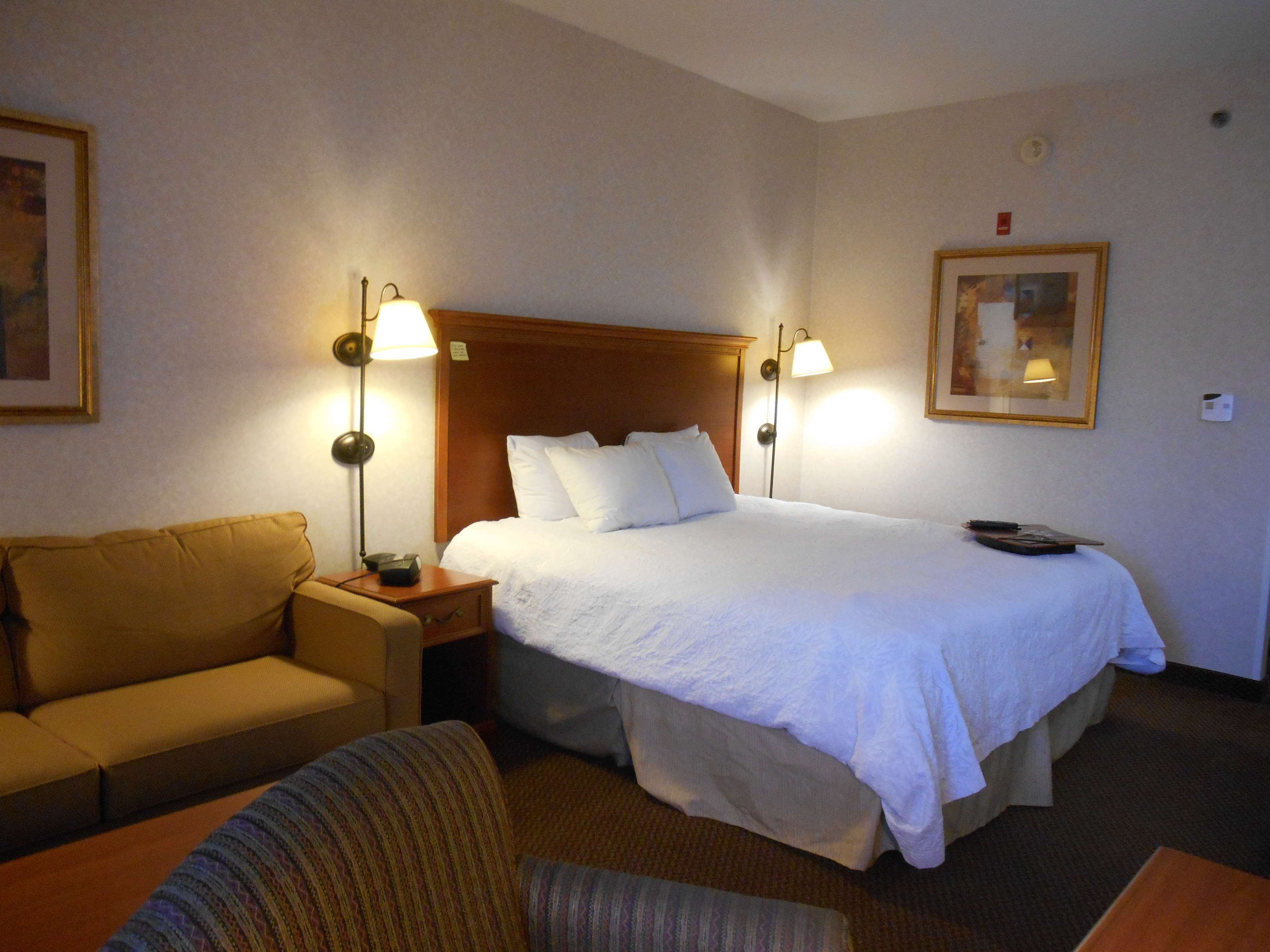 Una habitación de hotel con cama, sofá, mesita de noche y dos lámparas de pared.