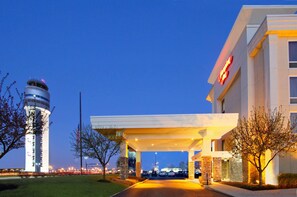 Een hotelentree met een modern ontwerp, een opvallende toren en een goed verlichte oprit.