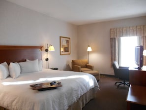 A hotel room with a large bed, a desk with a computer, a chair, and two lamps.