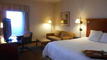 A hotel room with a bed, a desk with a computer, a chair, a sofa, and two lamps.