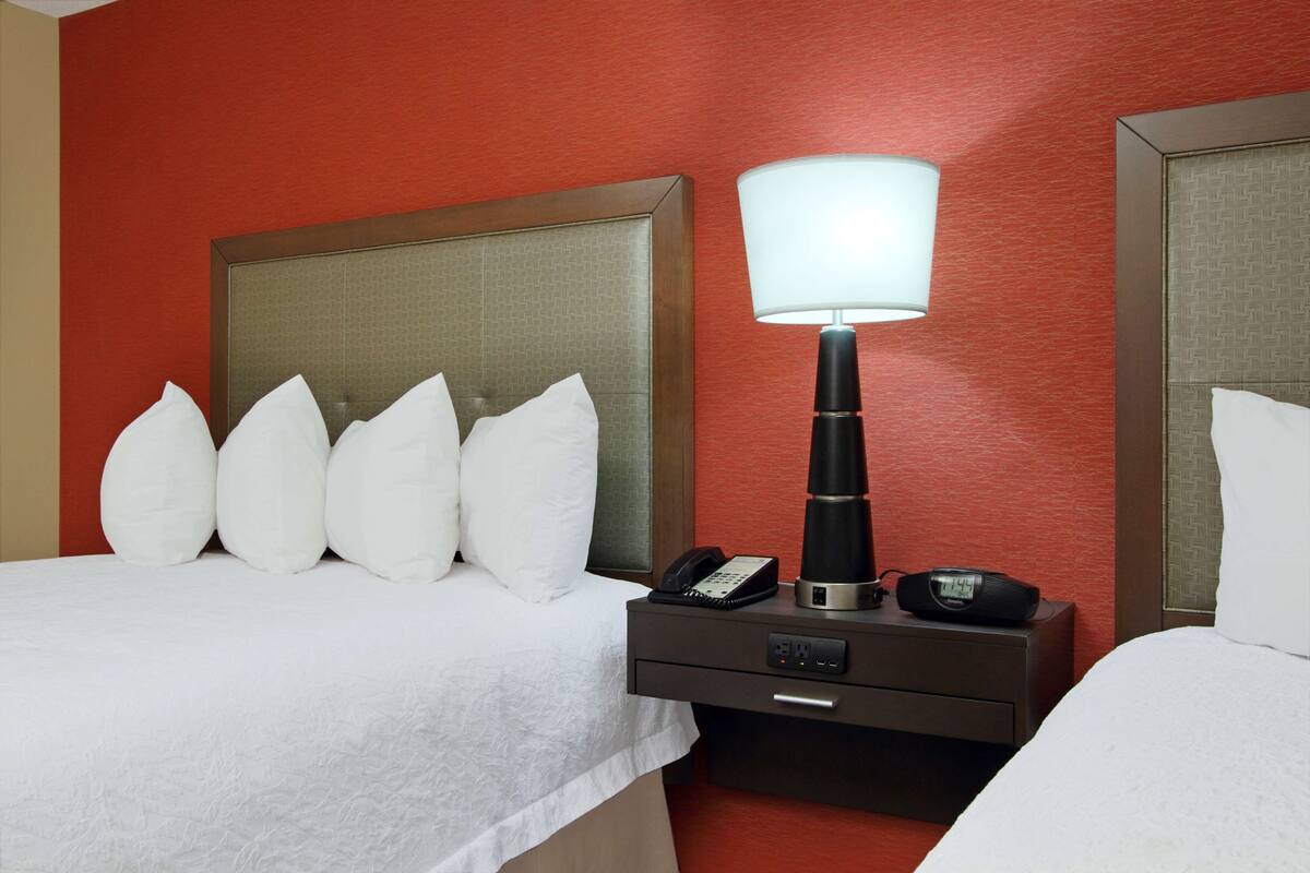 A hotel room with a bed, a bedside table with a lamp, a phone, and a clock.