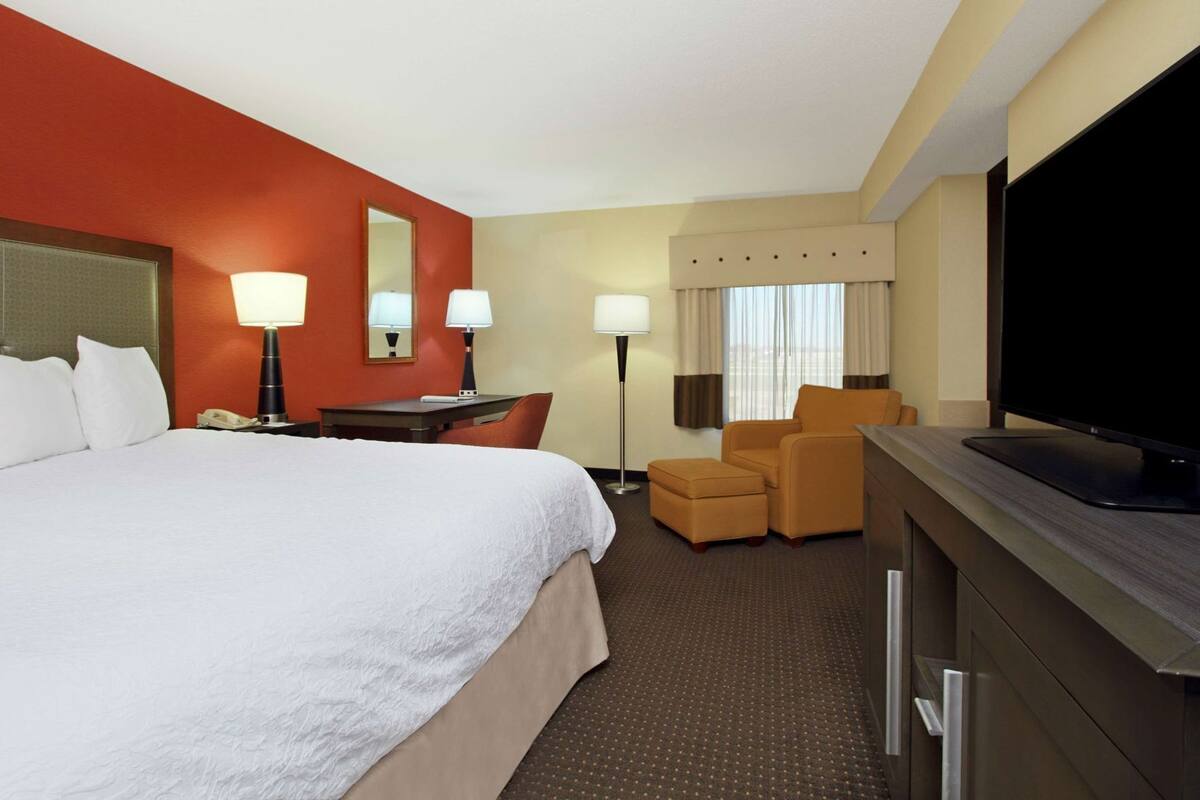 A hotel room with a large bed, a desk with a lamp, a television, and a chair.