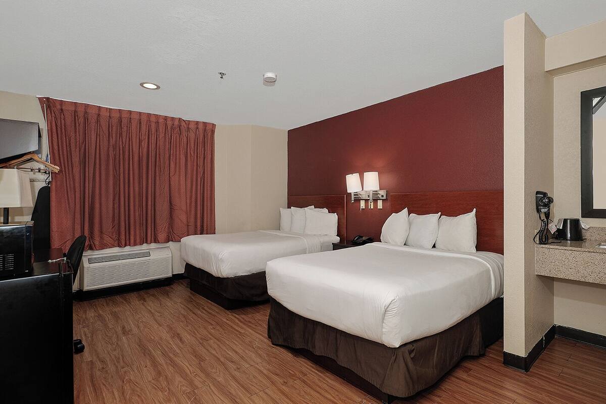 A hotel room with two beds, a desk with a computer, a telephone, and a mirror.