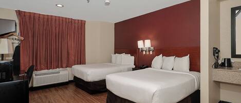 A hotel room with two beds, a desk with a computer, a telephone, and a mirror.