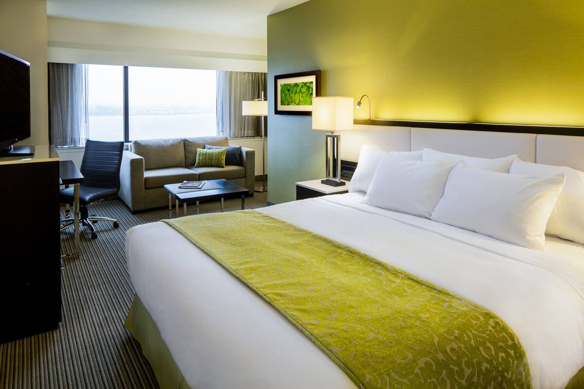 A hotel room with a large bed, a sofa, a desk, and a TV.