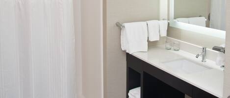 Un baño moderno con ducha, lavamanos, espejo y barra para toallas.