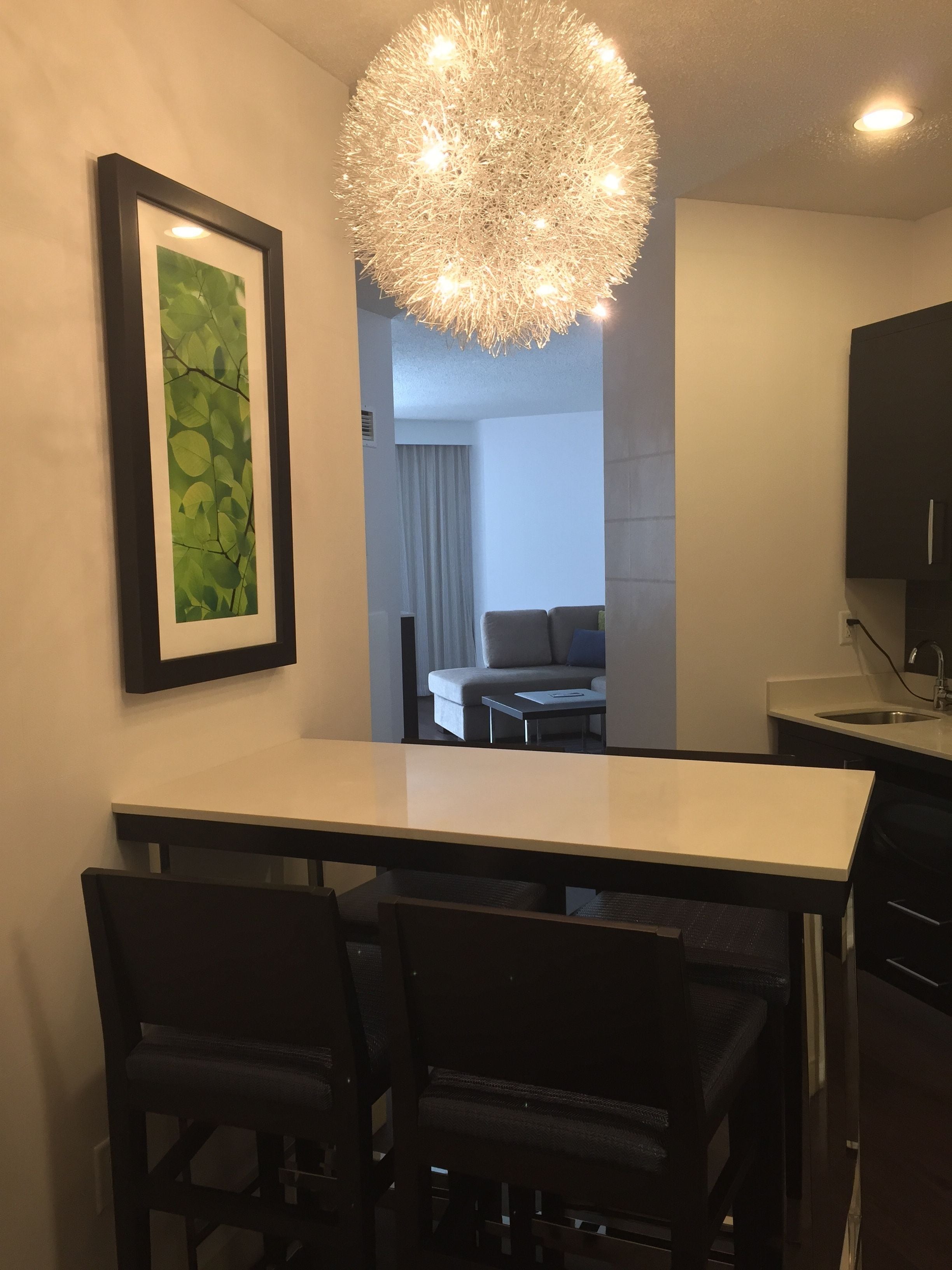 Een moderne keuken met een eethoek, met een kroonluchter, afbeeldingen in lijsten en uitzicht op een woonkamer.