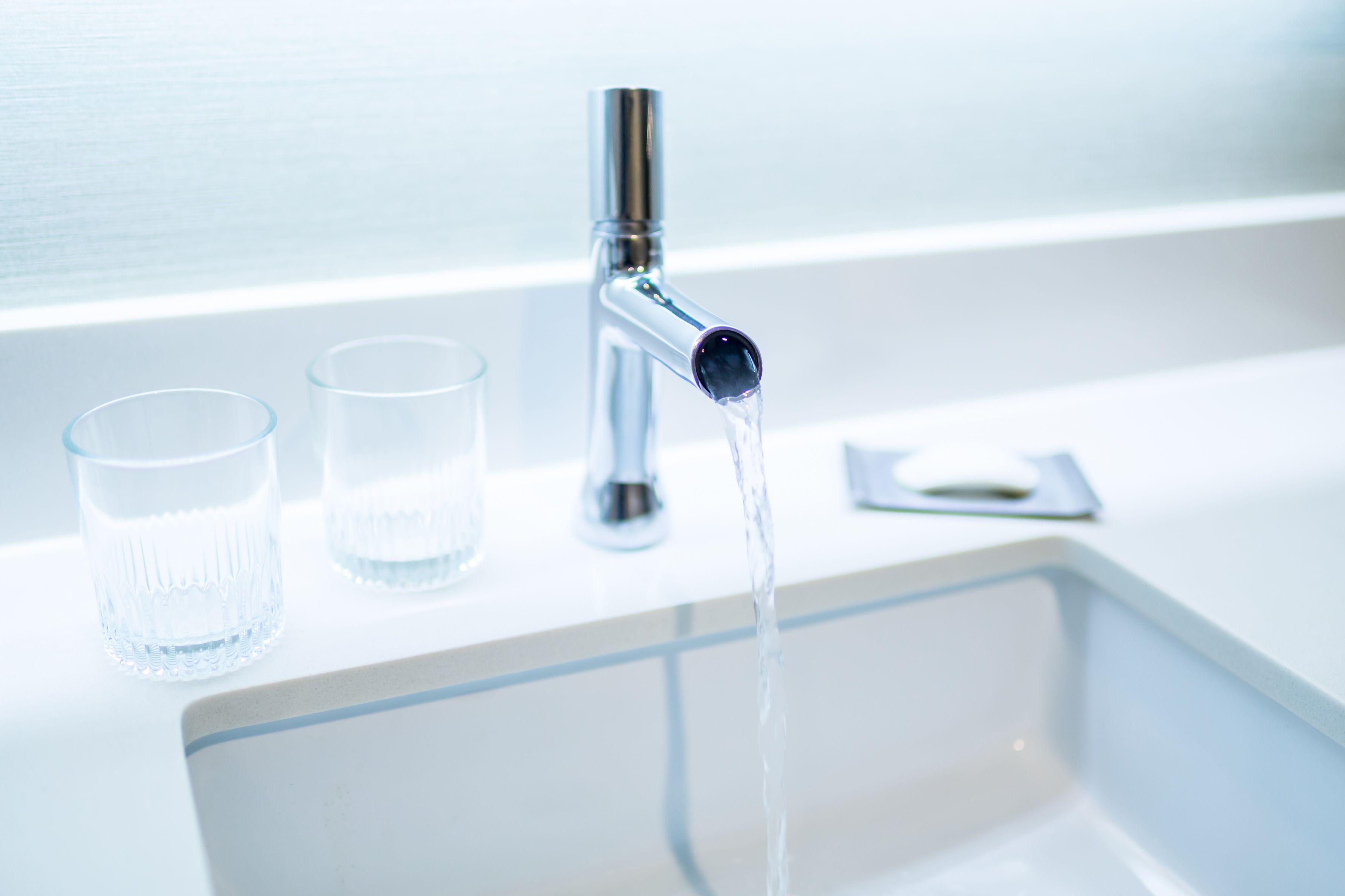 Un lavamanos moderno con un grifo y dos vasos con agua.
