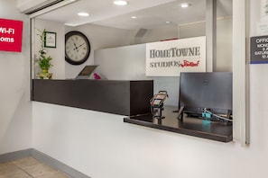 A reception desk with a clock, a sign for Home Townne Studios, and a Wi-Fi sign. - HomeTowne Studios & Suites by Red Roof Greensboro (Greensboro)
