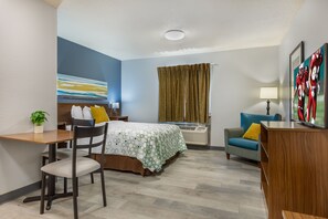 Una habitación de hotel con cama, escritorio, silla, televisión y ventana con cortinas.