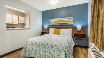 A hotel room with a bed, a nightstand with a lamp, a wall-mounted artwork, and a window with curtains.
