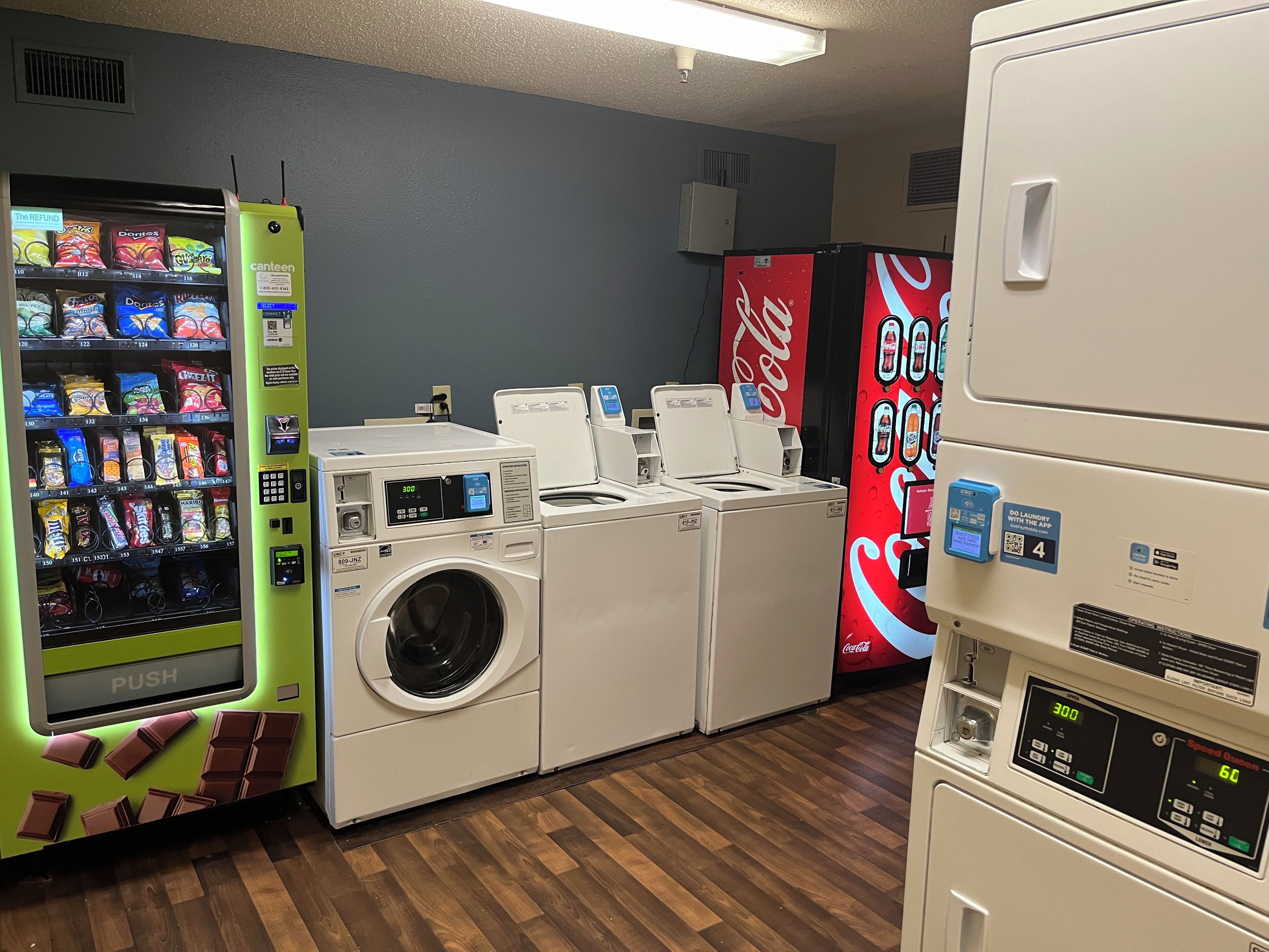 A laundry facility with a vending machine, washing machines, and a Coca-Cola refrigerator.