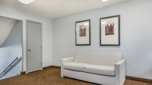 A room with a white sofa, two framed pictures on the wall, a door, and a wooden floor.
