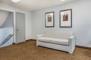 Une pièce avec un canapé blanc, deux tableaux encadrés au mur, une porte et un plancher en bois.