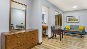 A room with a wooden dresser, a desk, a chair, a blue sofa with yellow cushions, and a framed picture on the wall.