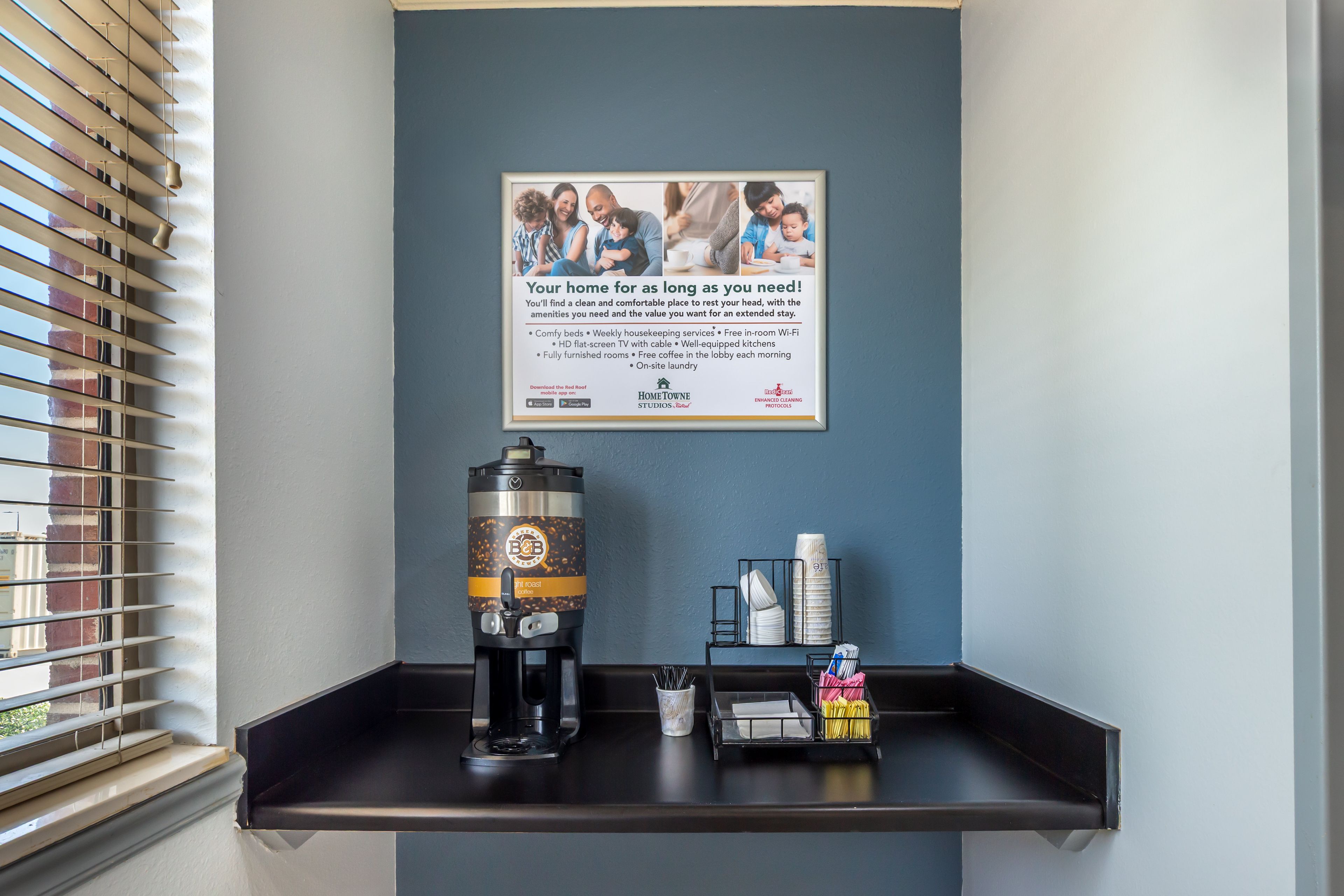 A wall-mounted sign with a family photo and text promoting home stay services, a coffee machine, and a tray with amenities.