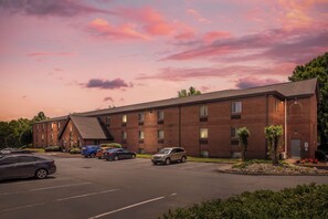 A multi-story brick building with a parking lot in front. - HomeTowne Studios & Suites by Red Roof Greensboro (Greensboro)