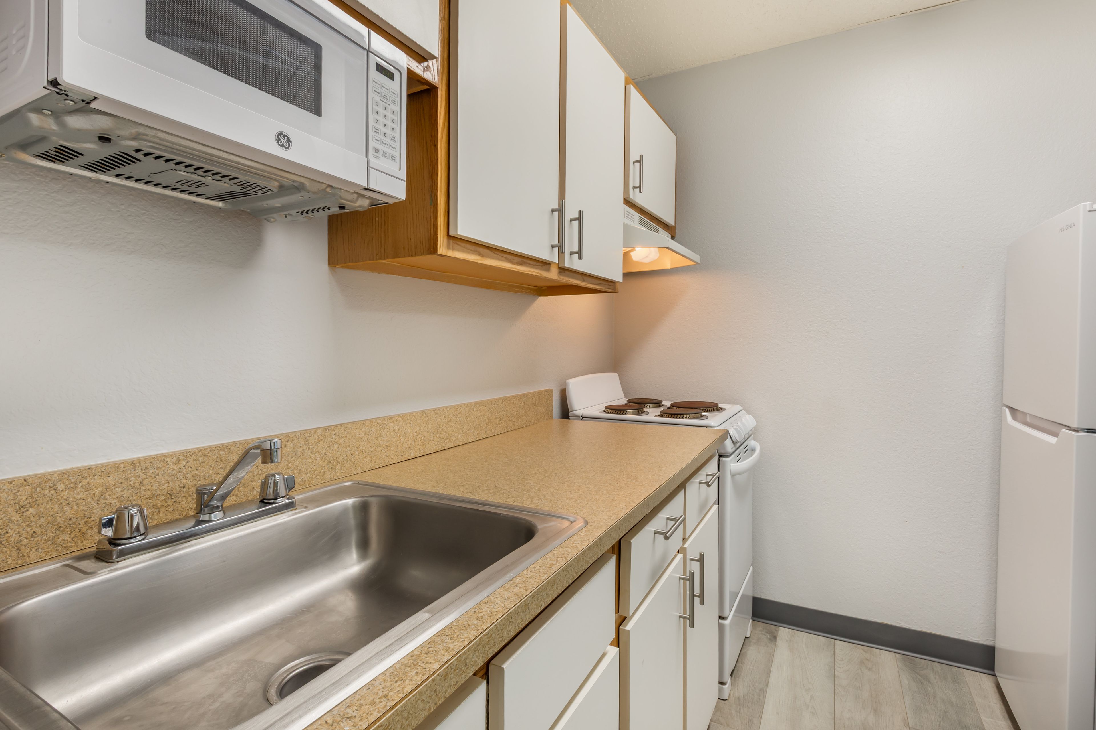 Una cocina con un lavamanos de acero inoxidable, armarios blancos, un microondas y un refrigerador.