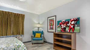 Una camera d'albergo con un letto, una sedia, una lampada, un televisore e un quadro appeso al muro.