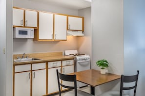 Una cocina compacta con armarios blancos, microondas, estufa, pileta y una mesa de comedor con dos sillas.