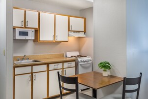 A compact kitchen with white cabinets, a microwave, a stove, a sink, and a dining table with two chairs.