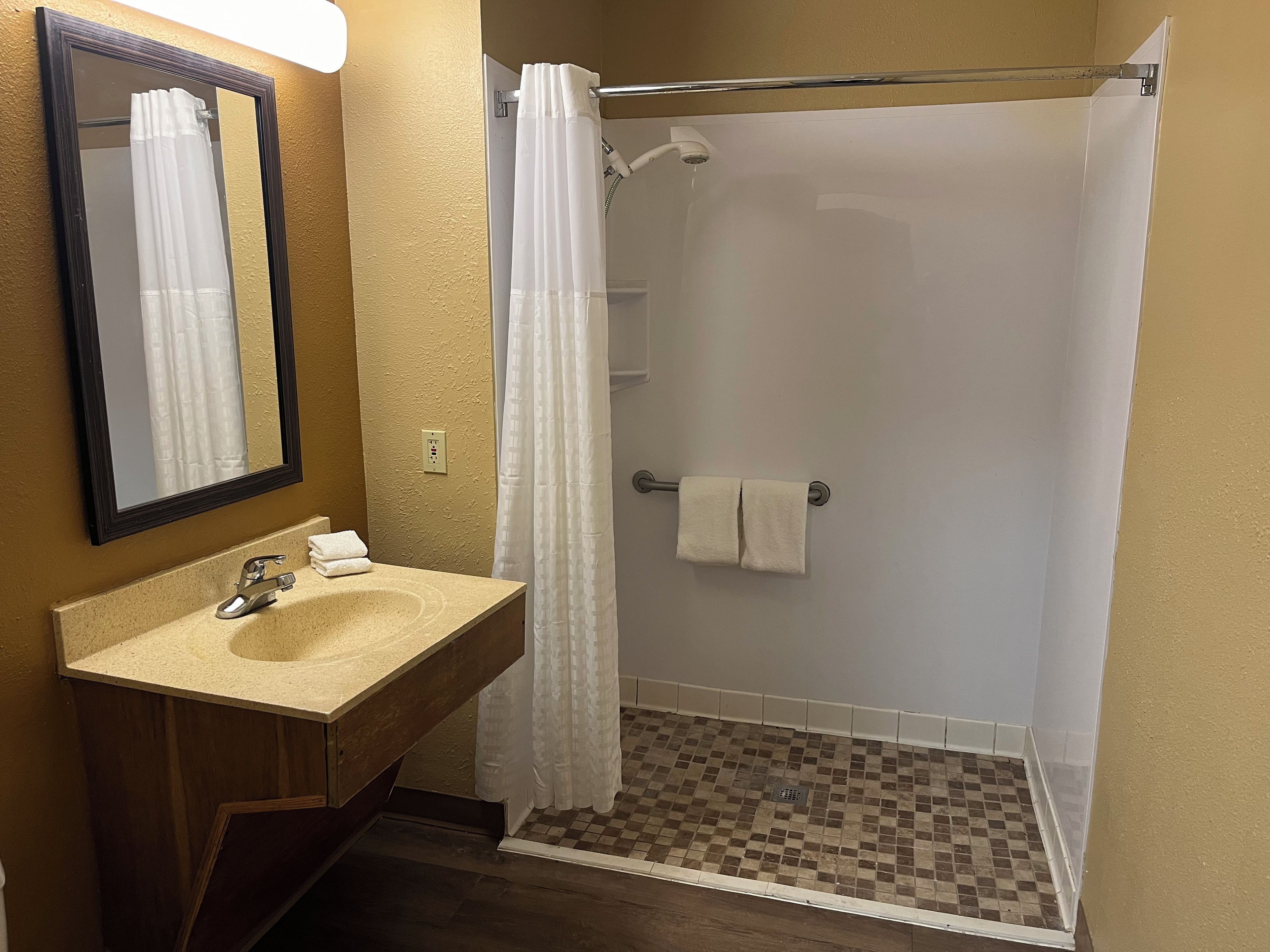 Un baño con lavabo, espejo, ducha y suelo de baldosas.