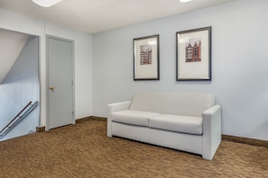 Una habitación con un sofá blanco, dos cuadros en la pared, una puerta y piso de madera.